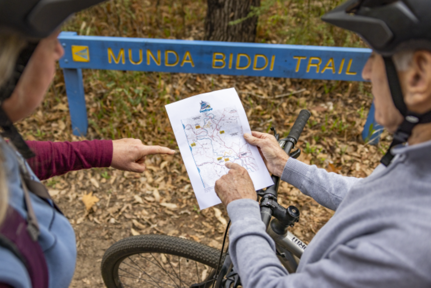 Riders planning route using official Munda Biddi Trail map near signpost